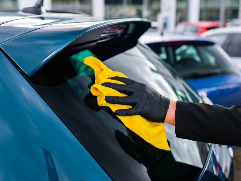 A service employee polishing the rear windscreen on a blue VW