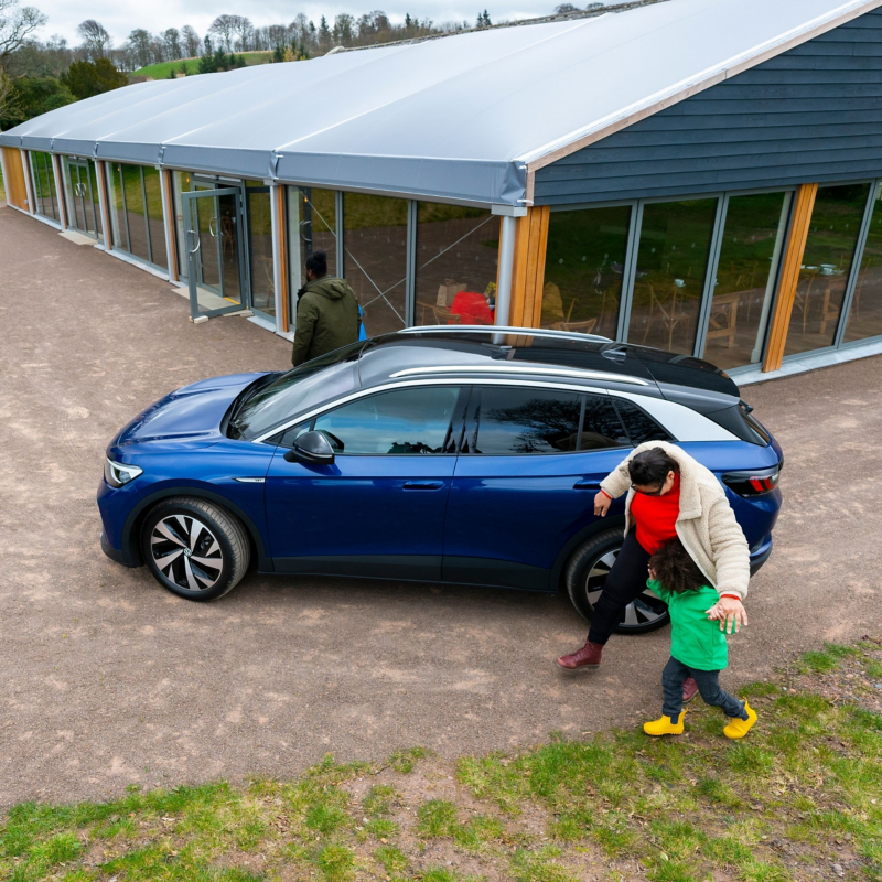 A family walking around a blue VW ID.4 parked outside a cafe