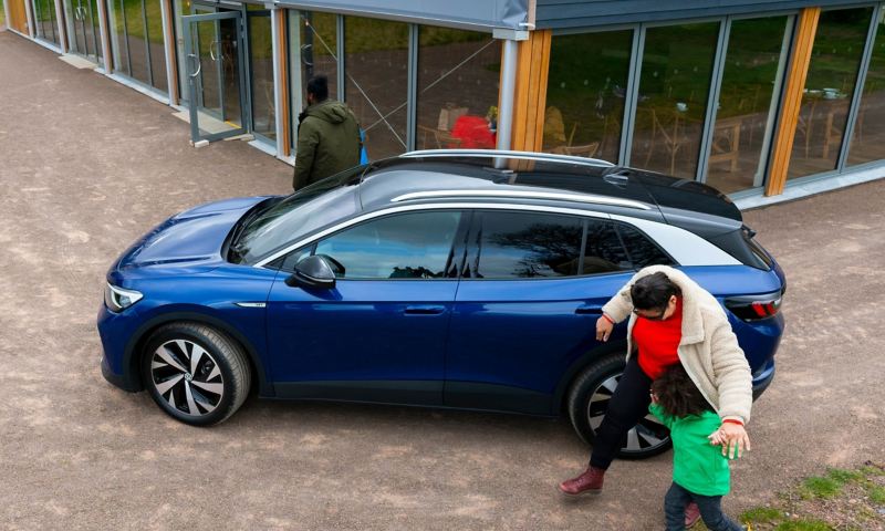A family walking around a blue VW ID.4 parked outside a cafe