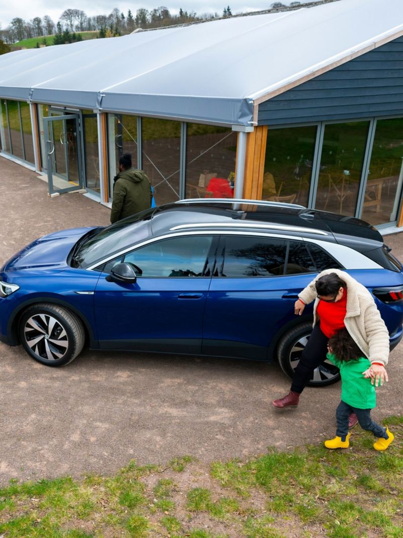 A family walking around a blue VW ID.4 parked outside a cafe