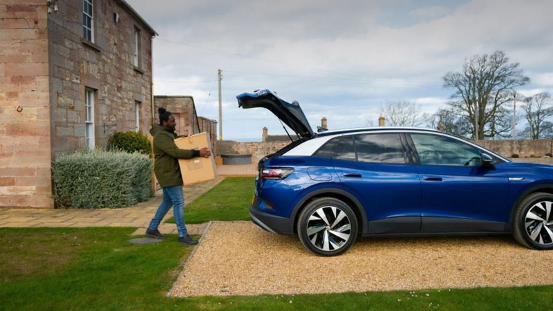 A person loading a parcel into the open boot of a blue VW ID.4