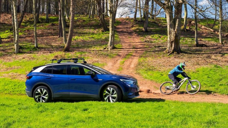 A parked blue VW ID.4 in a forest with a mountain biker in front