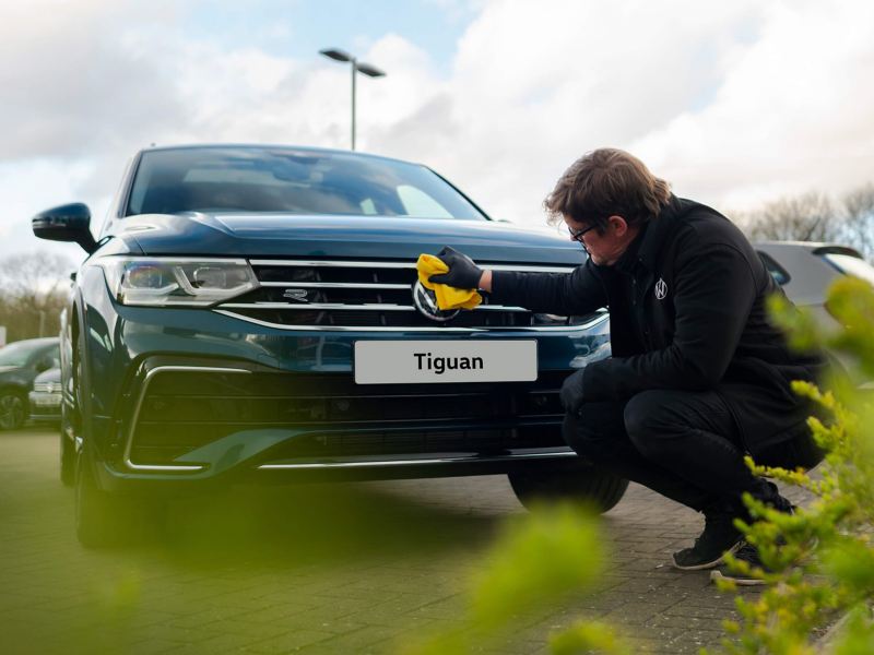 A service employee polishing the front badge on a blue VW Tiguan