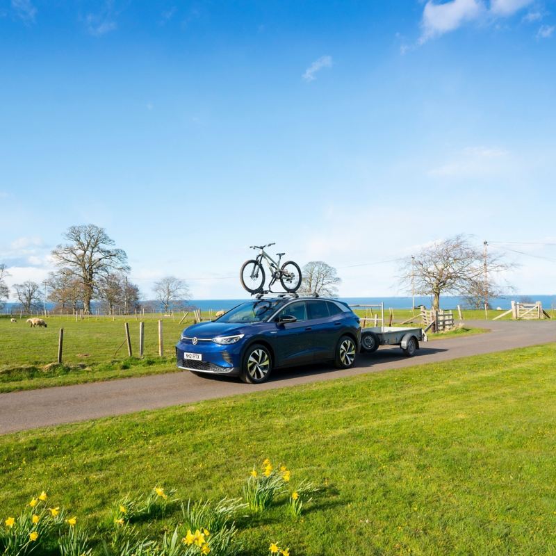 A blue VW ID.4 with roof bars towing a trailer