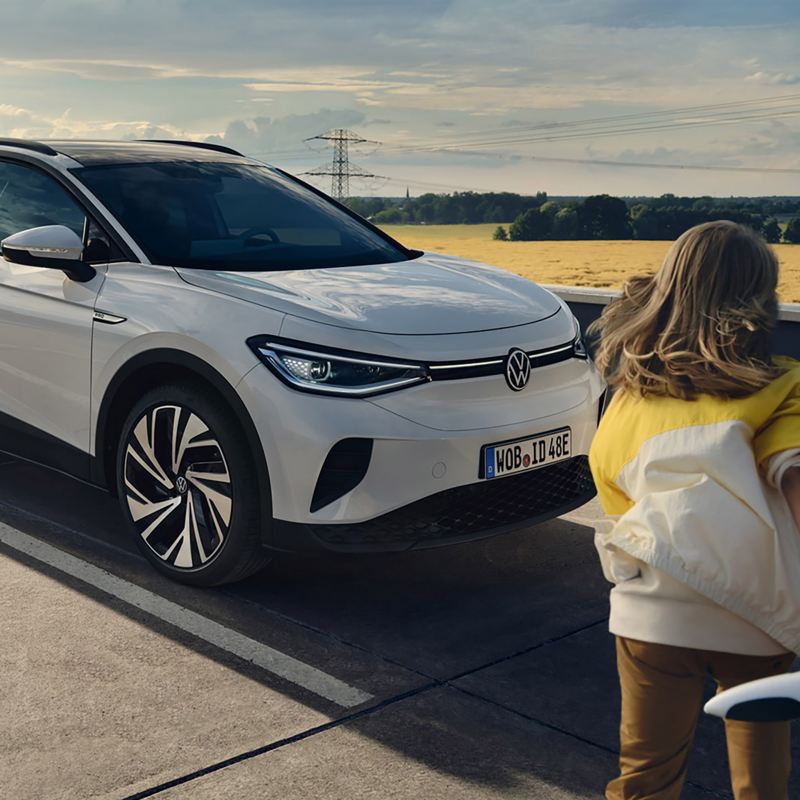 A woman walks to her parked VW ID.4, which is in a rural setting