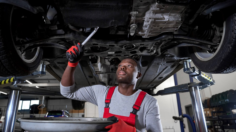 Man wearing red overalls and gloves working on a car