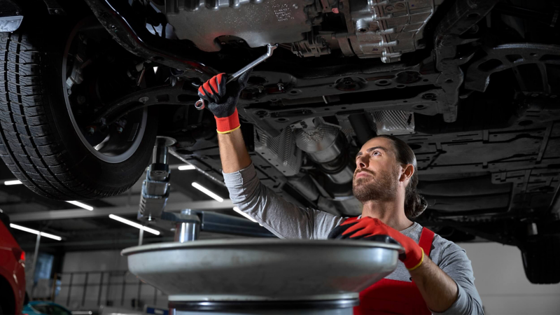 VW service employee under a vehicle checking the oil