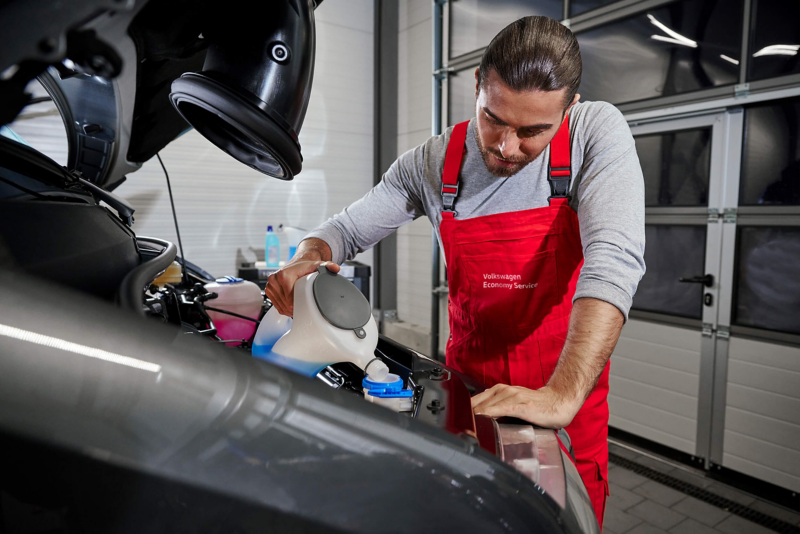 A VW service expert refilling washer fluid in the open bonnet of a vehicle.