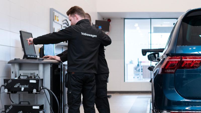 2 VW mechanics looking at a computer linked up to a car in a service centre