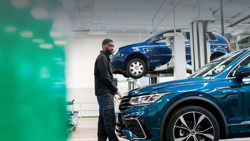 A technician stands at the front of a blue VW with hands on the bonnet