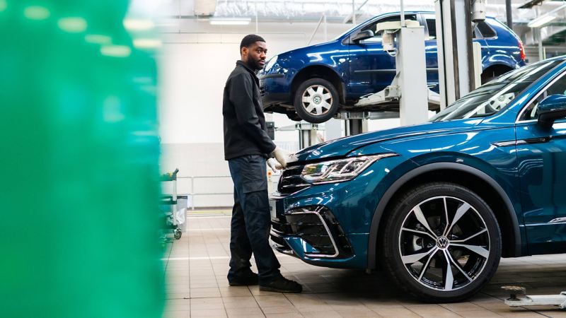 A technician holding about to open the bonnet of a blue VW Tiguan