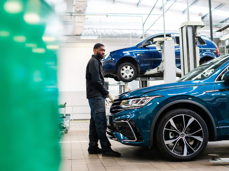 A technician stands at the front of a blue VW with hands on the bonnet