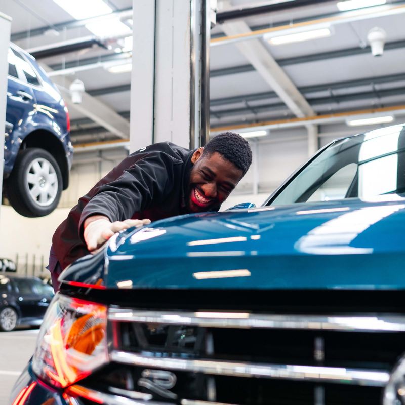 A technician inspecting the paintwork on a blue VW Tiguan