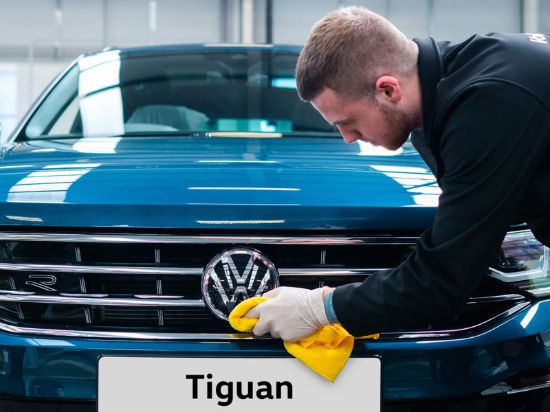 A technician buffering the front VW logo on a blue Tiguan