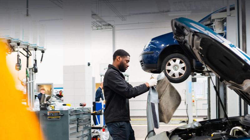 A VW technician stands looking into the engine bay of a car