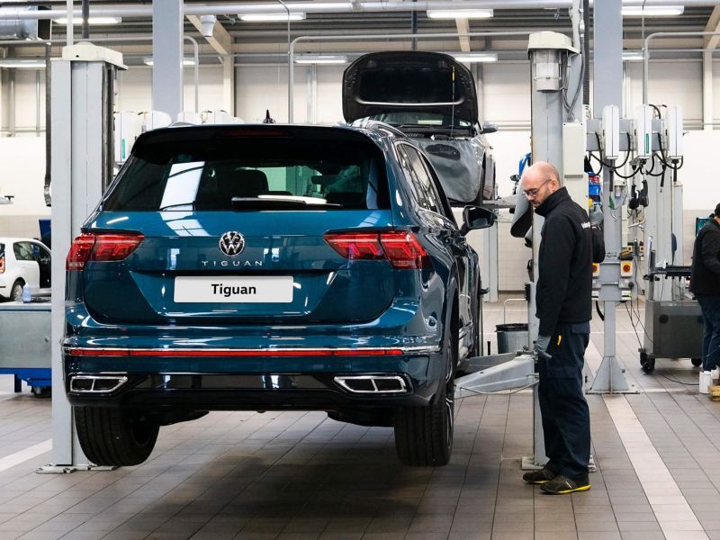 A blue VW Tiguan being raised on a ramp by a technician