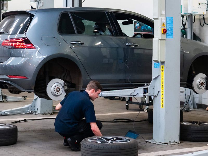 A VW technician knelt next to an exposed brake disc and pad
