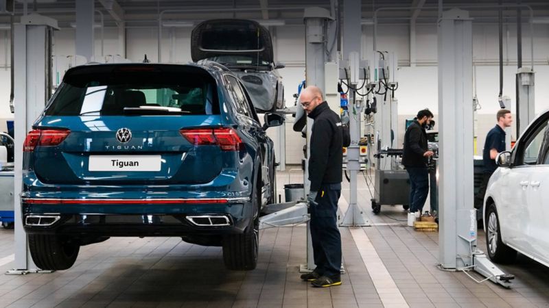 A technician stands next to a ramp raising a blue VW Tiguan