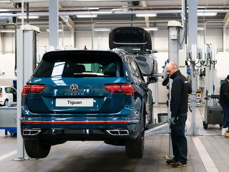 A technician stands next to a ramp raising a blue VW Tiguan