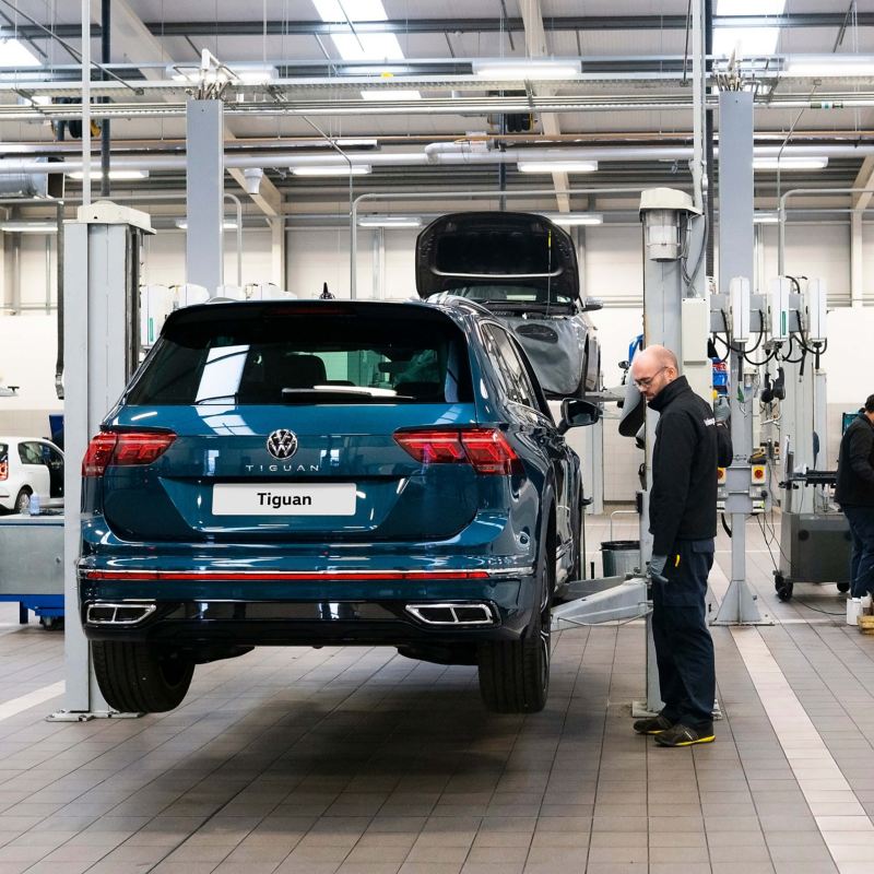 A technician stands next to a ramp raising a blue VW Tiguan