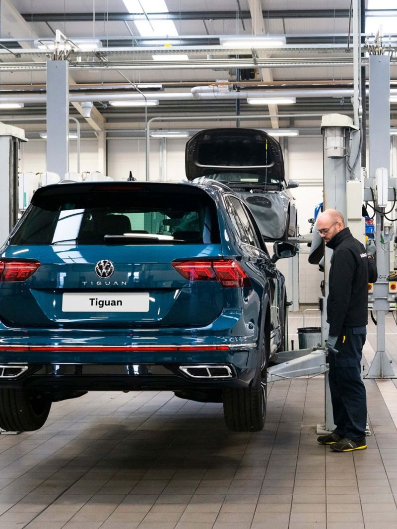 A technician stands next to a ramp raising a blue VW Tiguan