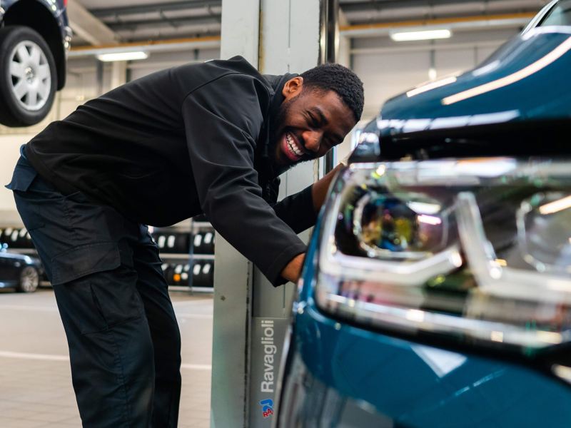 VW technician bent down next to a blue Tiguan next to the headlight