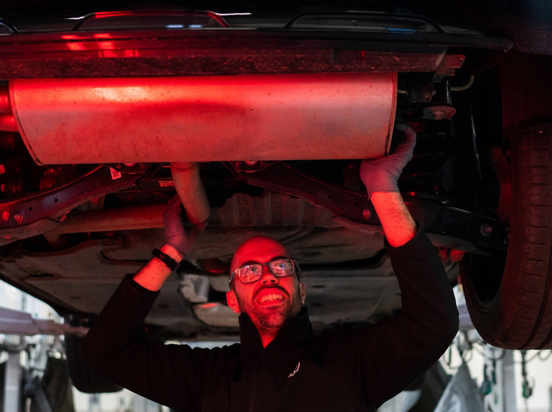 A VW technician inspecting the exhaust underneath the chassis of a car