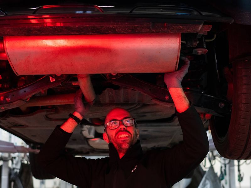 A VW technician inspecting the exhaust underneath the chassis of a car
