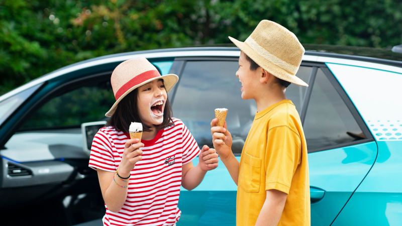 Two children eating ice cream in front of a parked Volkswagen car