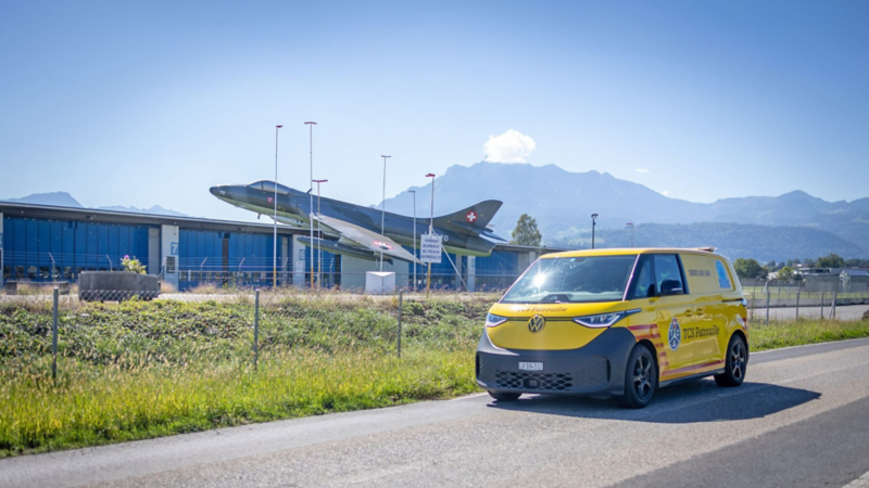 Gelber VW ID. Buzz der TCS Patrouille vor einem historischen Militärflugzeug in der Zentralschweiz.