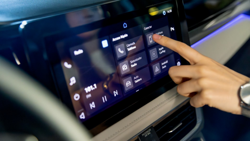 Mano sobre la pantalla táctil del sistema multimedia, con menú de funciones e iluminación azul.