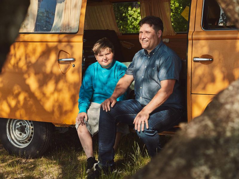 Far och son sitter vid sin VW campingbil