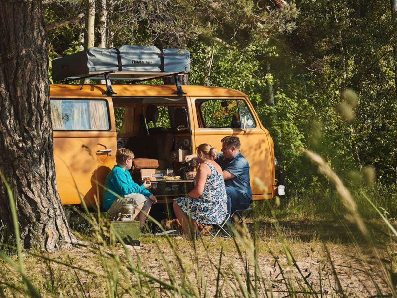 Familj fikar framför gul VW folkabuss campingbil