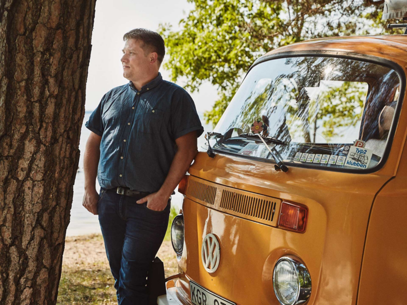 Man står vid sin gula VW folkabuss campingbil