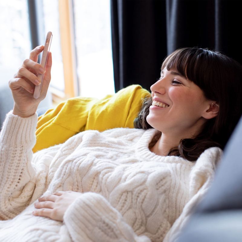 Une femme allongée regarde son smartphone en souriant.