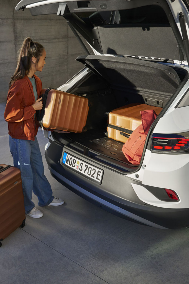 Volkswagen blanche avec le coffre ouvert. une femme charge le coffre du véhicule avec des valises.