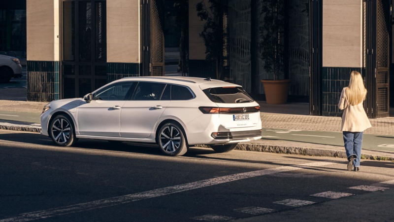 Une personne se tient debout, derrière une Passat eHybrid garée dans une rue.