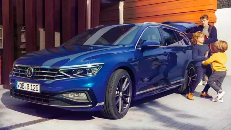VW Passat SW bleue garée avec une famille qui joue devant