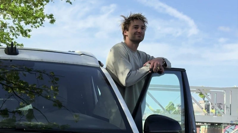 Pat Burgener è seduto nel suo VW California con la porta aperta e guarda fuori.