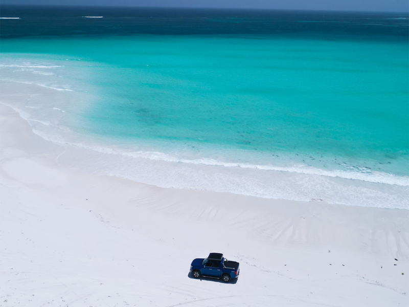 Ariel shot of VW Amarok driving on white sandy beach with ocean in background