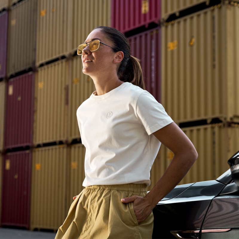 Mujer con prendas de Volkswagen Essentials frente a contenedores industriales.
