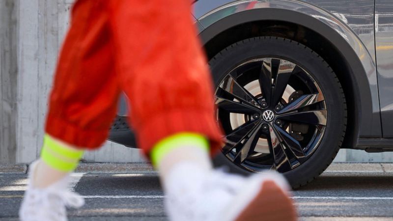 Vue au ras du sol du personne marchant au premier plan, avec le pneu d'une Volkswagen en arrière plan.