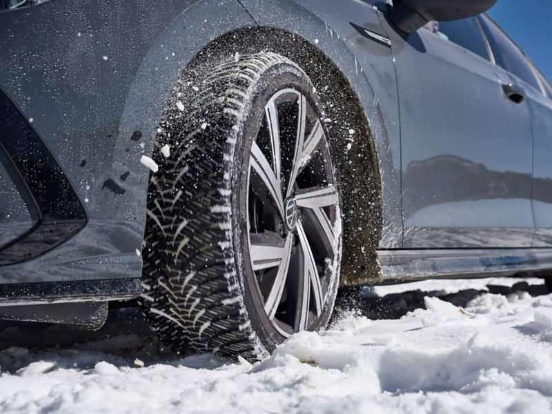 Gros plan sur la roue d'une voiture Volkswagen roulant dans de la neige tombée sur la chaussée.