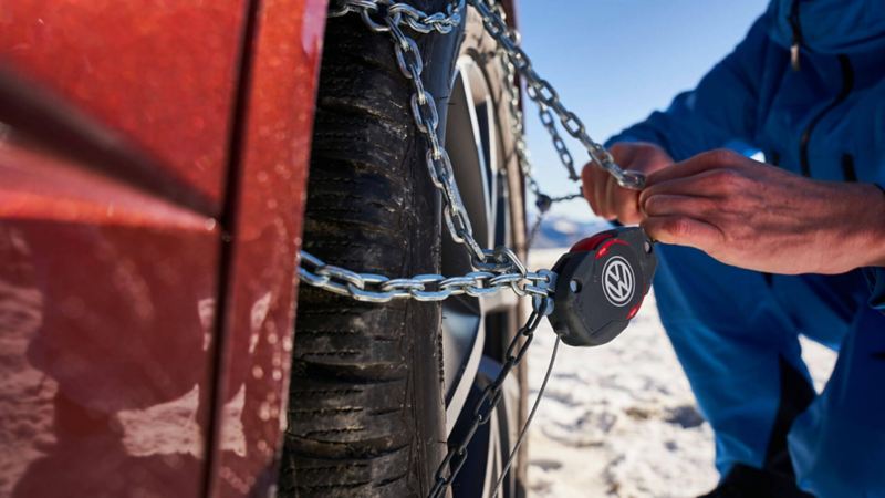 Un homme installe des chaines à neige sur la roue de sa Volkswagen.