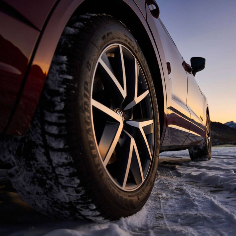 Gros plan sur une roue de Volkswagen, avec le véhicule arrêté sur un parking enneigé.