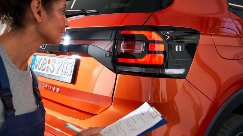 Une technicienne Volkswagen inspecte l'éclairage arrière d'un T-Cross pour un contrôle technique.