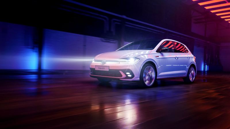 Shot of a white VW Polo GTI with LED headlights switched on, driving in a dark hall under light elements.