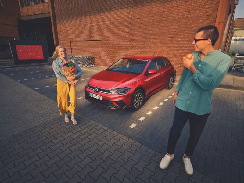 Volkswagen Polo rojo aparcado con personas delante sonriendo