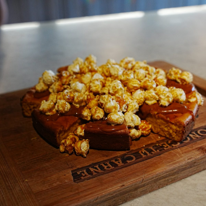Pastel redondo con cobertura de caramelo y abundantes palomitas caramelizadas sobre una tabla de madera.