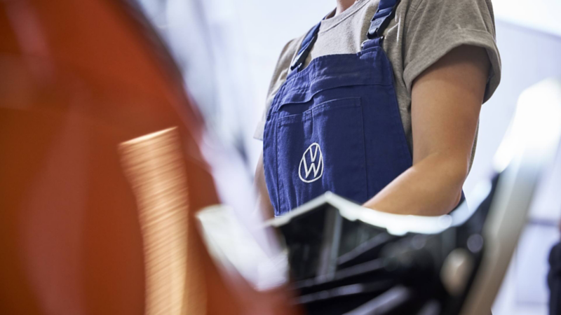 Técnica con overol azul y logo de Volkswagen revisa el motor de una camioneta.